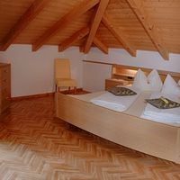 Ein gemütliches Schlafzimmer im Dachgeschoss mit sichtbaren Holzbalken, Doppelbett, Kommode und Glastür zum Balkon.