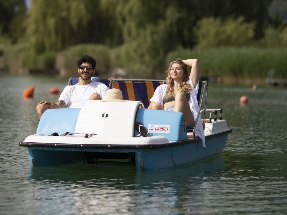 Ein Mann und eine Frau sitzen entspannt in einem Tretboot auf einem See.