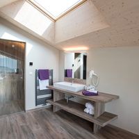 Helles Badezimmer mit bodengleicher Dusche, Waschbecken auf einem Holzwaschtisch und schräger Holzdecke mit großem Dachfenster.