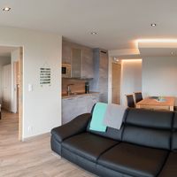 Helle, modern eingerichtete Ferienwohnung mit schwarzem Sofa, offener Küche, Esstisch und angrenzendem Schlafzimmer.