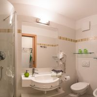 Helles, gefliestes Badezimmer mit Dusche, Waschbecken, Spiegel, Toilette und Bidet.