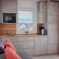 Moderne Küche mit grauen Schränken, Holzarbeitsplatte, Spüle, Kochfeld und Kaffeemaschinen; am Fenster hängen rote Vorhänge.