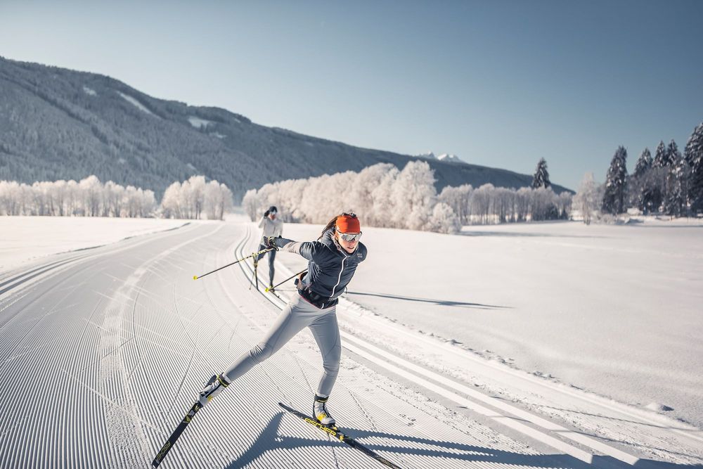 Zwei Langläufer trainieren auf einer präparierten Loipe in einer verschneiten Berglandschaft.