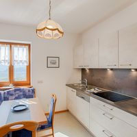 Helle Küche mit weißen Schränken, Herd, Spüle und Essecke vor einem Fenster mit Bergblick.