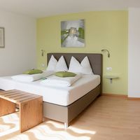 Helles Schlafzimmer mit Doppelbett, grünen Akzenten, Holzschrank und kleinem Holztisch.