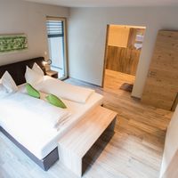 Modernes Schlafzimmer mit zwei zusammengestellten Einzelbetten, weißer Bettwäsche, grünen Kissen und Holzmöbeln; eine offene Tür führt in den angrenzenden Raum.