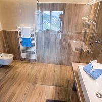 Modernes Badezimmer mit Holzoptik-Fliesen, Glasdusche, Badewanne, Waschbecken und Handtüchern.