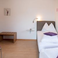 Helles Zweibettzimmer mit zwei weiß bezogenen Betten, Holzmöbeln und rosa Vorhängen.