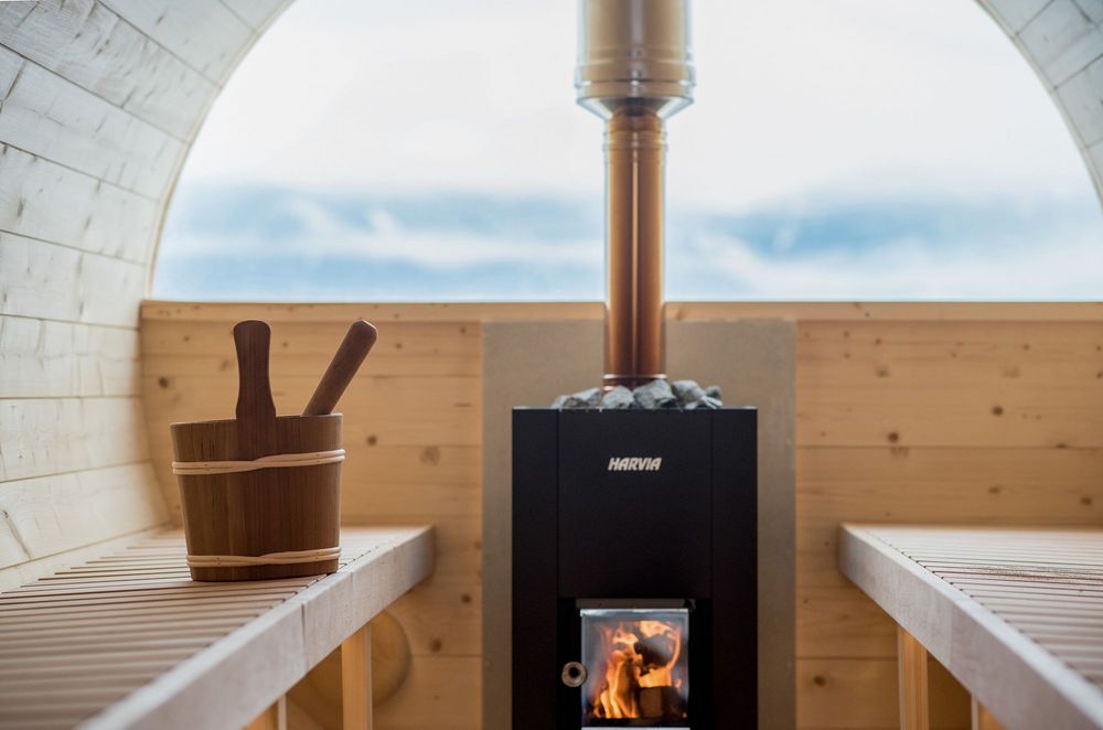 Holzsauna mit einem brennenden Saunaofen, Steinen und einem Holzeimer mit Kelle auf der Bank.