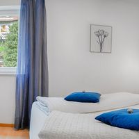 Helles Schlafzimmer mit großem Doppelbett, weißen Kissen, blauen Akzenten und einem Fenster mit blauen Vorhängen.