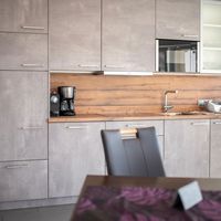 Moderne Küche mit grauen Schränken, Holzarbeitsplatte und Rückwand, Kaffeemaschine, Spüle und Mikrowelle.