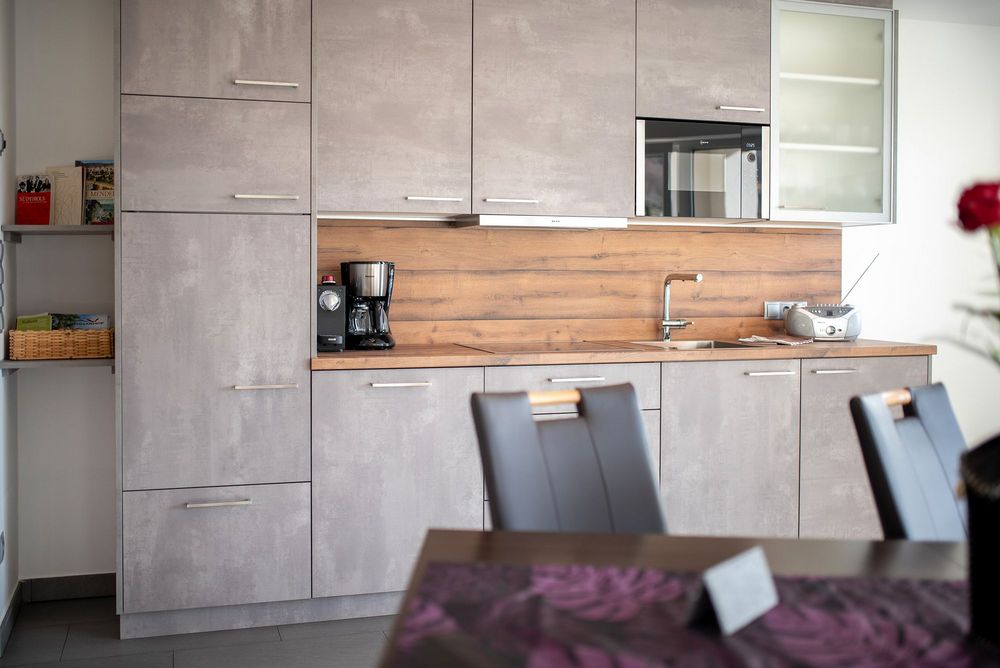 Moderne Küche mit grauen Schränken, Holzarbeitsplatte und Rückwand, Kaffeemaschine, Spüle und Mikrowelle.