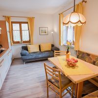 Heller Wohn- und Essbereich mit Küchenzeile, grauem Sofa, Holztisch mit Äpfeln und gelben Vorhängen.