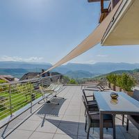 Sonnige Dachterrasse mit Esstisch, Stühlen und Hängematte vor einer weiten Berglandschaft.