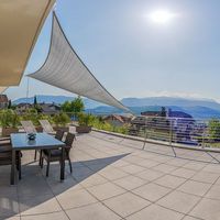 Große möblierte Terrasse mit Sonnensegel und weitem Blick auf ein Dorf und die Berge.