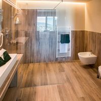 Modernes Badezimmer mit Walk-in-Dusche aus Glas, Badewanne, Waschbecken und Handtuchheizkörper; durch das Fenster sind Berge zu sehen.