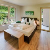 Helles Schlafzimmer mit Doppelbett, weißen Kissen, grünen Akzenten und großem Fenster zum Garten.