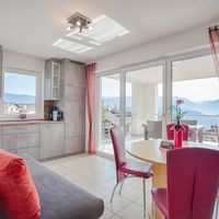 Heller Wohn- und Essbereich mit Küchenzeile, Sofa und großen Glastüren zum Balkon mit Blick auf die Berge.