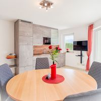 Heller Wohnküchenbereich mit grauen Einbauschränken, rundem Esstisch und Terrassentür zum Garten.