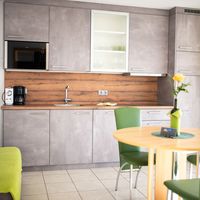 Helle Wohnküche mit grauen Schränken, Holzarbeitsplatte, Esstisch mit grünen Stühlen und grüner Couch.