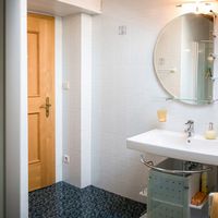 Helles Badezimmer mit Dusche, Waschbecken, rundem Spiegel und türkisfarbenem Unterschrank unter einer Dachschräge.