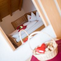 Blick durch eine Tür in ein gemütliches Schlafzimmer mit Holzbalkendecke, weiß bezogenem Bett und einem Präsentkorb im Vordergrund.