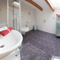 Helles Badezimmer im Dachgeschoss mit Waschbecken, Dusche, WC und roten Handtüchern.