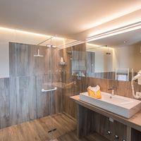 Modernes Badezimmer mit bodengleicher Glasdusche, Waschbecken, großem Spiegel und warmen Holzfliesen.