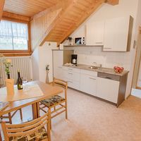 Helle Dachgeschosswohnung mit Holzbalkendecke, kleiner Küchenzeile und gedecktem Esstisch.