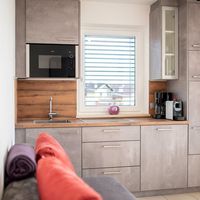 Moderne Küchenzeile mit grauen Schränken, Holzarbeitsplatte, Spüle, Mikrowelle und Kaffeemaschine vor einem Fenster.