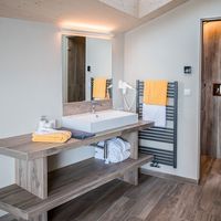 Modernes Badezimmer mit Waschtisch aus Holz, großem Spiegel, Handtuchheizkörper und Dusche.