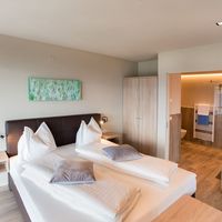 Helles Schlafzimmer mit zwei zusammengeschobenen Einzelbetten, Nachttischen und offenem Zugang zum Badezimmer.