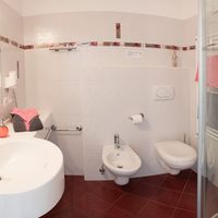 Helles Badezimmer mit Waschbecken, Bidet, Toilette und Dusche; rosafarbene Handtücher und Accessoires setzen Akzente.