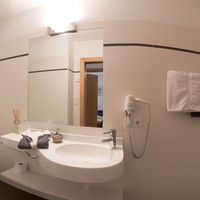 Helles Badezimmer mit Waschbecken, großem Spiegel, Toilette, Handtüchern und gläserner Dusche.