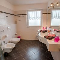 Helles Badezimmer mit Dusche, Bidet, Toilette, zwei Waschbecken und großem Spiegel.