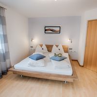 Helles Schlafzimmer mit einem Doppelbett, blauen Kissen, gestreiften Vorhängen und einer Holztür.