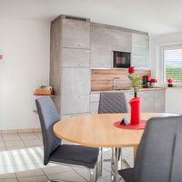 Heller Wohn- und Essbereich mit grauer Küche, rundem Esstisch, Sofa und großen Fenstern zur Terrasse.