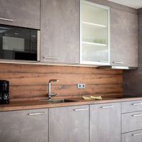 Moderne Küche mit grauen Schränken, Holzarbeitsplatte, Spüle, Mikrowelle und Kaffeemaschinen.